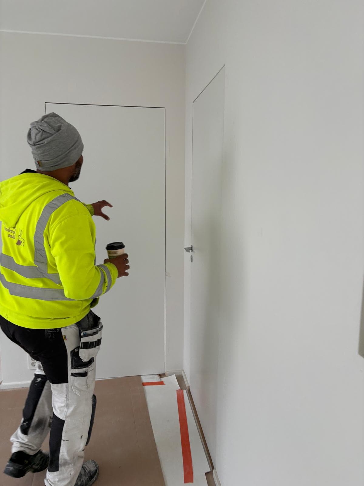 Målare i varselkläder framför nymålade vita väggar i en villa.